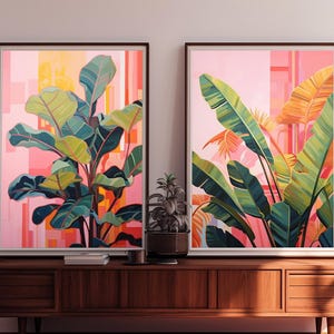 May include: Two framed botanical art prints. One features a large plant with green and blue leaves against a pink and orange background. The other print shows large green and yellow leaves with a pink and orange background. The prints are displayed on a wooden cabinet.
