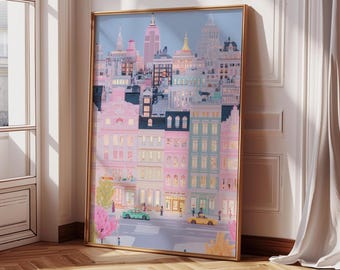 May include: A framed art print depicting a stylized cityscape with buildings in shades of pink, blue, and white. The artwork features a gold frame and includes a street scene with small cars and figures. The overall theme is a whimsical urban landscape.