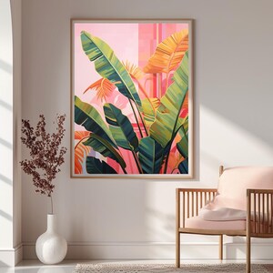 May include: A framed art print featuring a vibrant illustration of tropical banana leaves in shades of green, yellow, and orange against a pink background. The artwork is displayed in a light-colored wooden frame, adding a touch of nature-inspired decor.