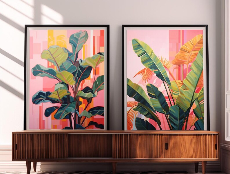 May include: Two framed botanical art prints. One features a large plant with green and yellow leaves against a pink and orange background. The other print shows large green and orange leaves against a pink background. The frames are black.