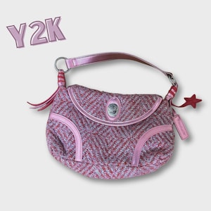 Puede incluir: Bolso de mano tejido rosa y blanco con forma curva, con cierre de solapa y cierre plateado. El bolso tiene ribetes de cuero rosa y un asa a juego. Un charm en forma de estrella roja y el texto "Y2K" son visibles.