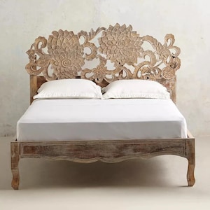 May include: A white wooden bed frame with a carved floral headboard. The headboard features intricate details and a distressed white finish.