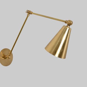 1-light cone wall fixture in raw brass. Mid-century modern Sputnik design adds vintage charm and sleek elegance to any interior space