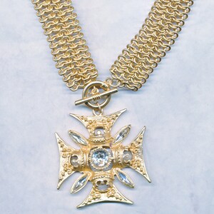 May include: A gold chain necklace with a large, ornate cross pendant. The cross has four clear crystal stones set in the center and around the edges.