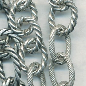 May include: A close-up of a silver chain necklace with a twisted rope design. The chain is made of metal and has a shiny finish.