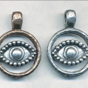 May include: Two silver eye charms with a beaded border, one charm is in a bronze setting and the other is in a silver setting.