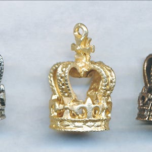 Może przedstawiać: Trzy miniaturowe korony w różnych wykończeniach: srebrne, złote i brązowe. Każda korona ma otwór w kształcie serca i skomplikowane detale.