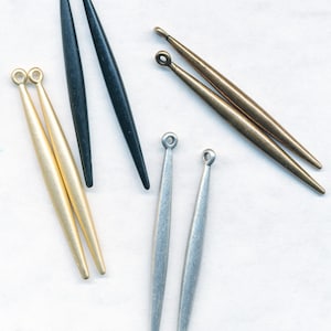 May include: Set of six metal earring findings in black, gold, and silver. The findings are long and slender with a pointed tip.