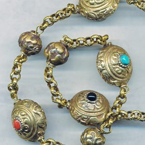 Puede incluir: Un collar de cadena de oro con cuentas redondas y ovaladas. Las cuentas est&aacute;n decoradas con dise&ntilde;os intrincados y engastadas con piedras preciosas azules, turquesa, negras y rojas.