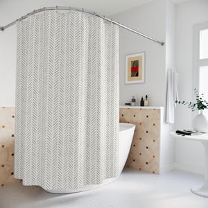 May include: A white shower curtain with a black herringbone pattern hangs from a curved, silver-colored rod. The bathroom has a white tub, a small table, and a framed artwork with red and black accents.