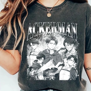 May include: A charcoal gray short-sleeve t-shirt featuring a graphic print of the anime character Levi Ackerman in various poses. The text ACKERMAN LEVI is printed in a bold, distressed white font above the black and white character illustrations.
