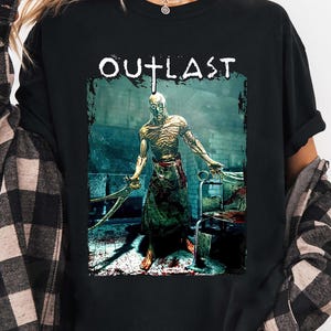Puede incluir: Camiseta negra con la palabra "OUTLAST" sobre un gr&aacute;fico de un personaje de juego de terror sosteniendo herramientas quir&uacute;rgicas. El personaje est&aacute; en un quir&oacute;fano sangriento.