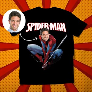 May include: Black t-shirt with the text "SPIDER-MAN" in red and white letters. A superhero figure in a red and blue suit with a mask is shown on the shirt. The superhero's face is replaced with a person's face.