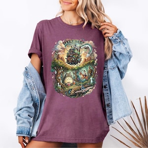 May include: A maroon t-shirt featuring a colorful graphic design. The design depicts a fantasy scene with a castle, characters, and creatures. The shirt is worn with a blue denim jacket.