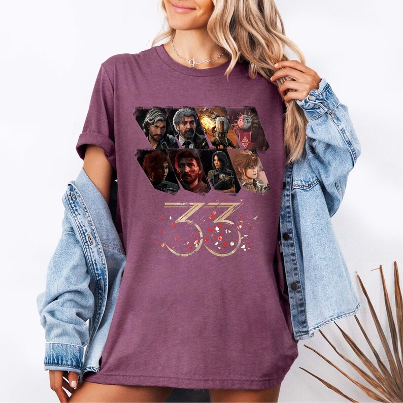 May include: A maroon t-shirt featuring a graphic design with multiple character portraits and the number "33" in gold. Red and white confetti-like shapes are scattered around the number. The shirt is made of a soft material.