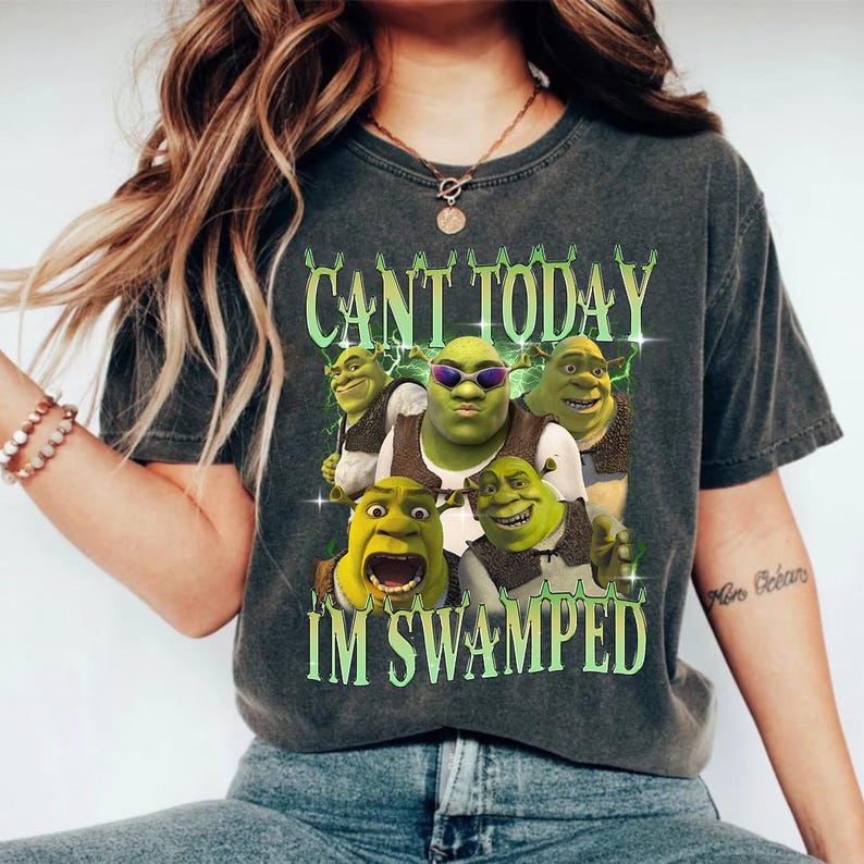 May include: A dark gray t-shirt with a graphic print of Shrek characters. The text on the shirt reads "Can't today I'm swamped".