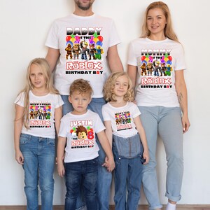 May include: A family of five wearing white t-shirts with a Roblox theme. The shirts feature the text "Daddy of the Roblox Birthday Boy", "Mommy of the Roblox Birthday Boy", "Brother of the Roblox Birthday Boy", "Sister of the Roblox Birthday Boy", and "Justin the Roblox Birthday Boy".
