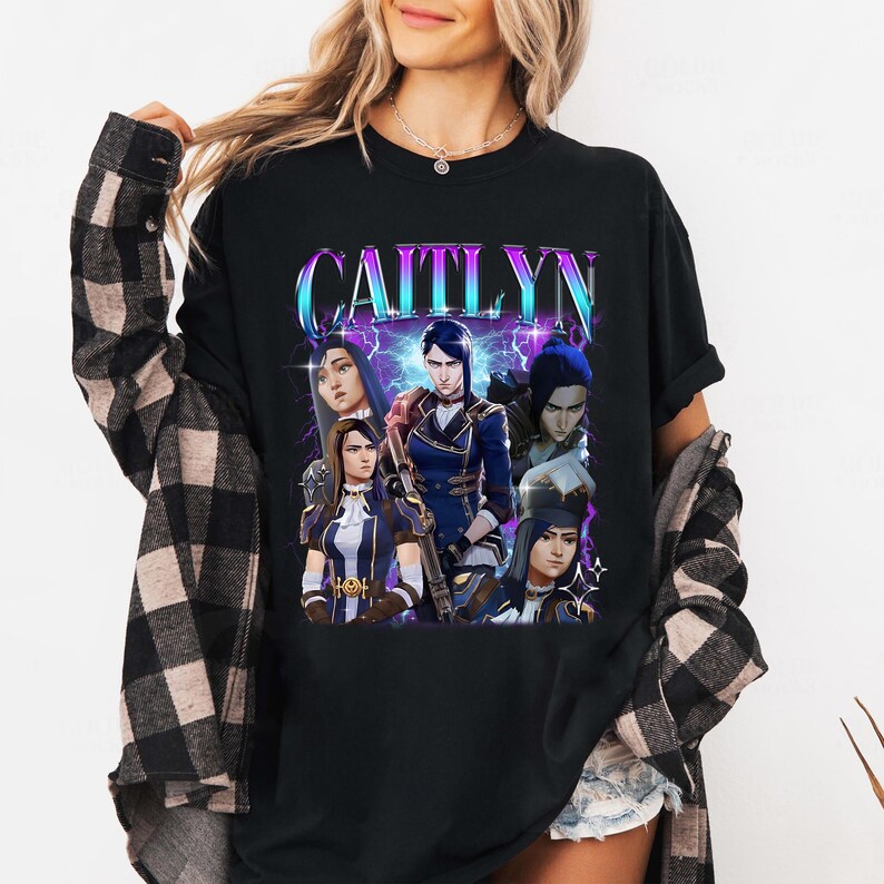 May include: Black t-shirt with a graphic print of a group of characters from the video game League of Legends. The text "CAITLYN" is printed in a large, bold font above the characters.