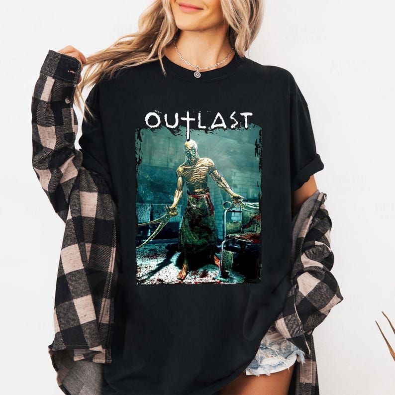 Puede incluir: Camiseta negra con la palabra "OUTLAST" sobre un gr&aacute;fico de un personaje de juego de terror sosteniendo herramientas quir&uacute;rgicas. El personaje est&aacute; en un quir&oacute;fano sangriento.