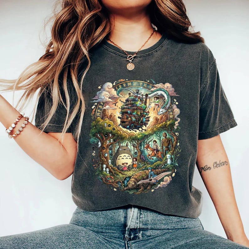 May include: Dark grey t-shirt featuring a colorful illustration of a fantasy scene with a castle, characters, and forest elements. The design is circular, with detailed artwork and a vintage wash appearance.