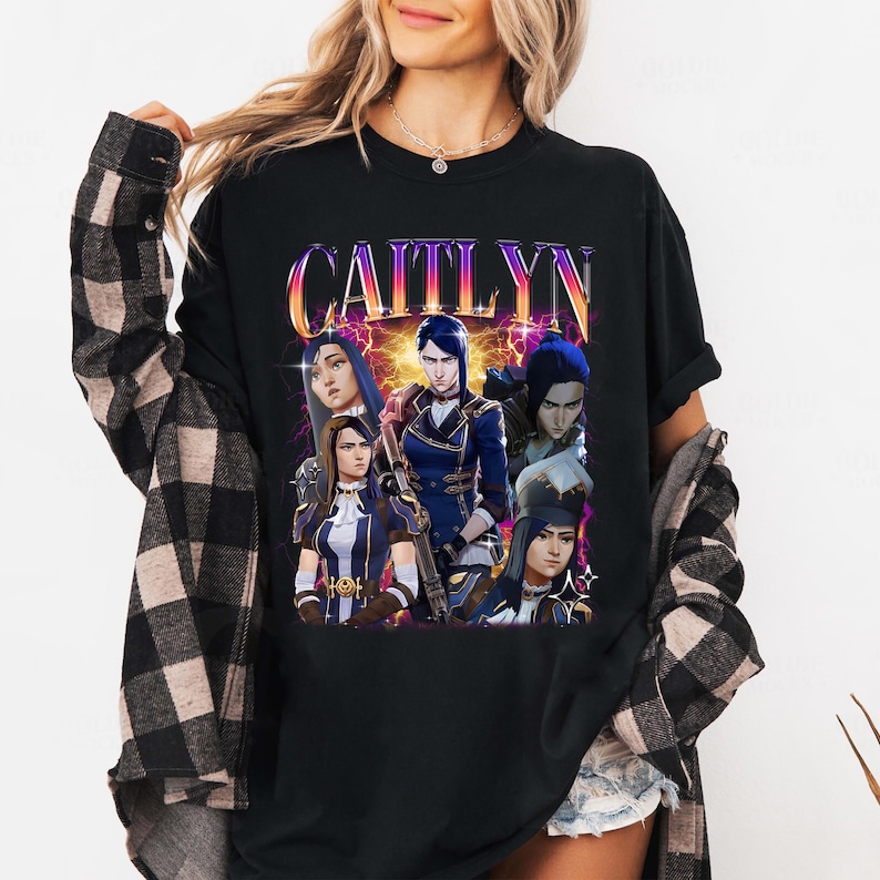 May include: Black t-shirt with a graphic print of a group of characters from the video game League of Legends. The text "Caitlyn" is printed in large, colorful letters above the characters.