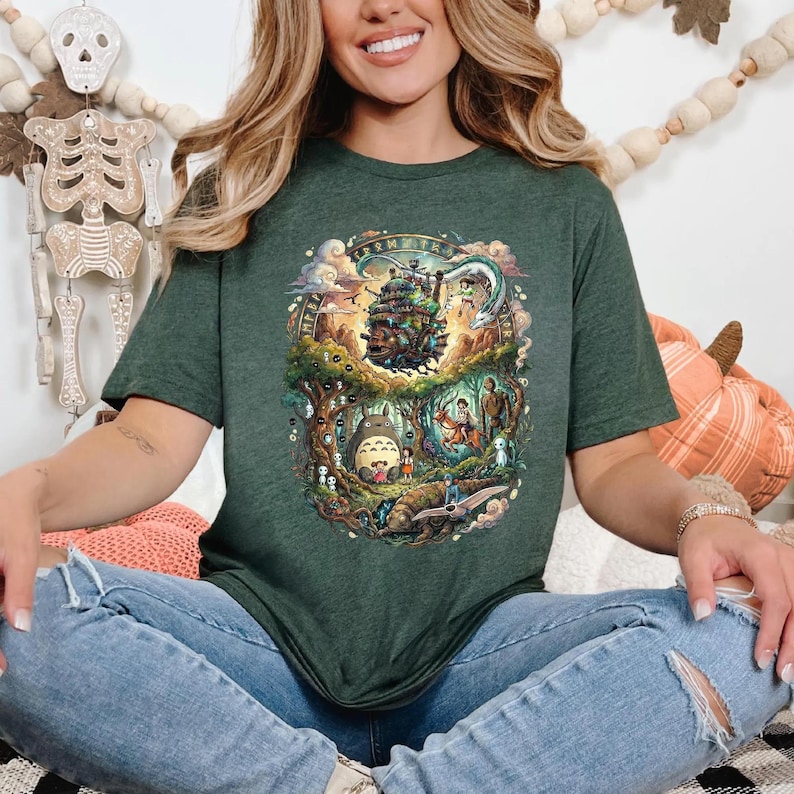 May include: Dark green t-shirt featuring a colorful graphic design with characters and scenes from a popular animated film. The design includes a castle, forest, and various creatures. The shirt is made of a soft material.