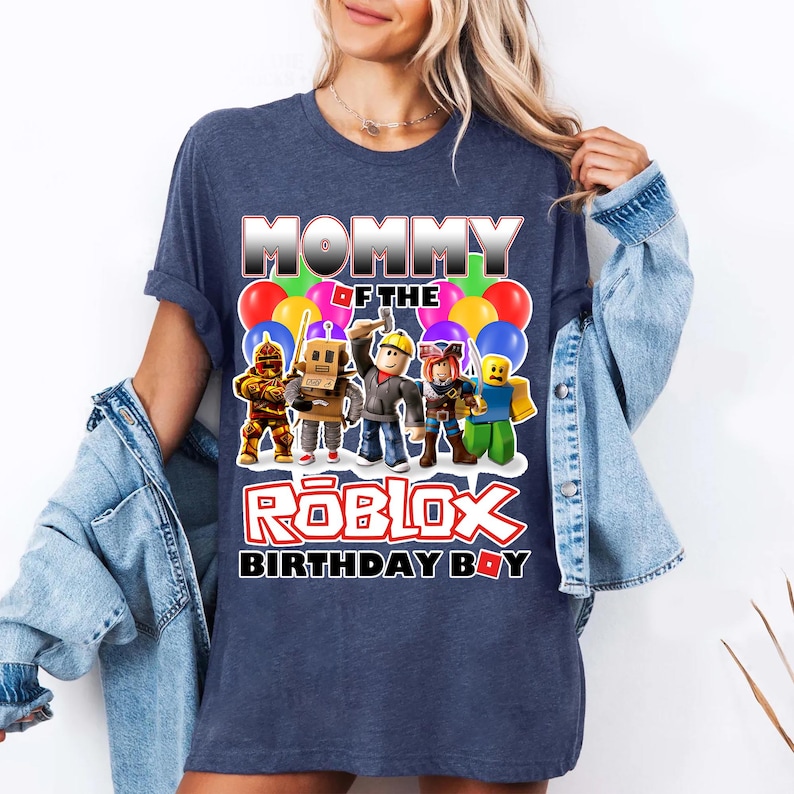 May include: A navy blue t-shirt with the text "Mommy of the Roblox Birthday Boy" in white and red letters. The shirt features a graphic of Roblox characters with colorful balloons.