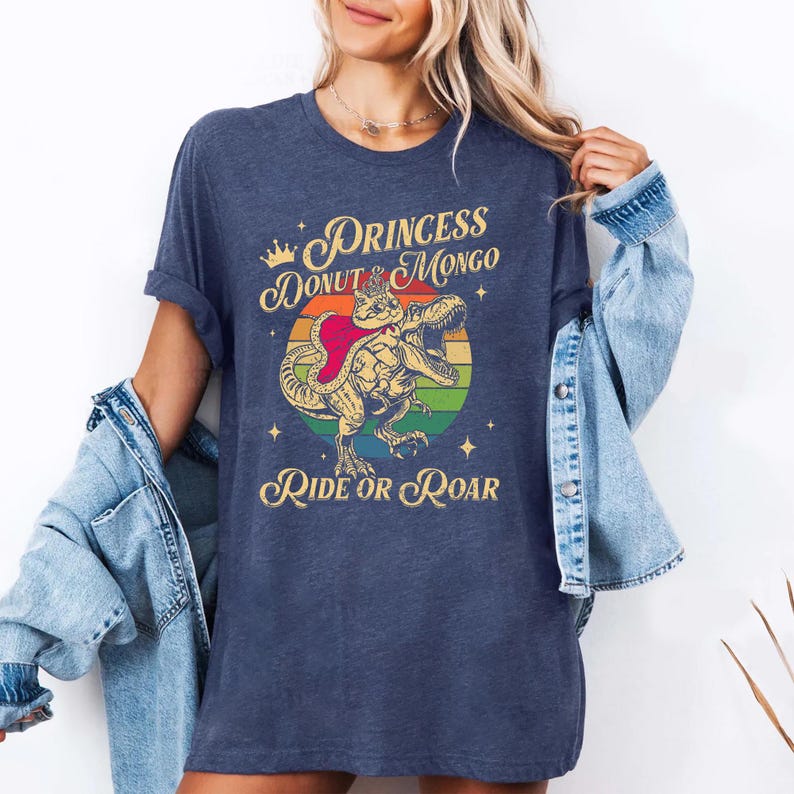 Puede incluir: Camiseta azul marino con un dise&ntilde;o de dinosaurio con el texto "Princess Donut & Mongo Ride or Roar". El dise&ntilde;o incluye un c&iacute;rculo arco&iacute;ris y estrellas.