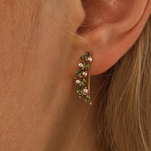 May include: A pair of gold earrings with a curved design featuring green and white gemstones.