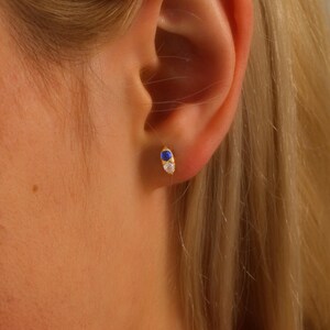 May include: A pair of gold stud earrings with a blue and white gemstone design.