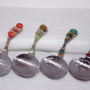 May include: Four silver spoons with decorative handles made of beads in various colors, including red, green, blue, and brown. The spoons have different designs on the bowl.