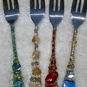 May include: Four silver forks with decorative beaded handles. The handles are decorated with colorful beads, including turquoise, red, white, and gold.