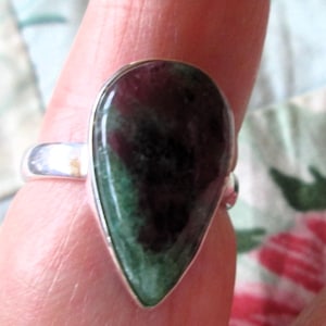 May include: A silver ring with a teardrop-shaped green and purple gemstone.