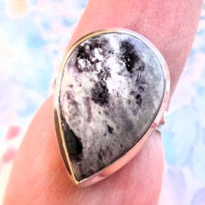 May include: A silver ring with a teardrop-shaped black and white gemstone. The gemstone has a swirling pattern.