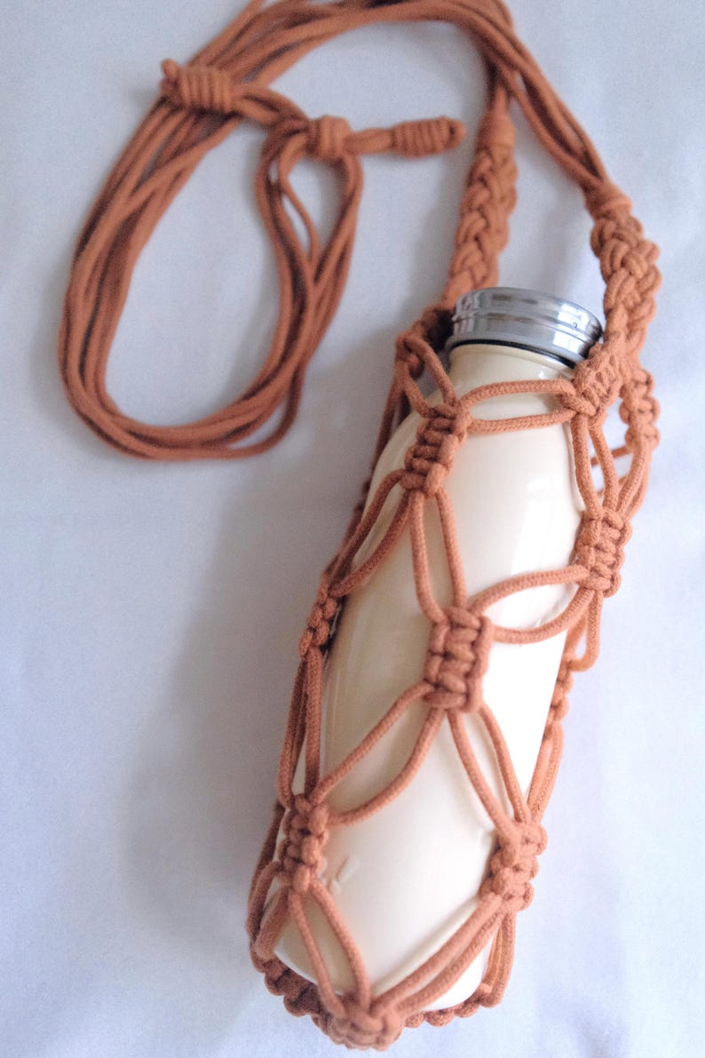 Pu&ograve; includere: Un porta bottiglia in crochet marrone con una bottiglia d'acqua bianca all'interno. Il porta bottiglia ha una lunga tracolla per portarlo sulla spalla.