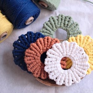 Pu&ograve; includere: Cinque sottobicchieri in macram&eacute; di diversi colori, tra cui blu, marrone, bianco, verde e giallo. I sottobicchieri sono circolari e hanno un design rialzato e testurizzato.