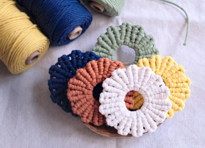 Pu&ograve; includere: Cinque sottobicchieri in macram&eacute; di diversi colori, tra cui blu, marrone, bianco, verde e giallo. I sottobicchieri sono circolari e hanno un design rialzato e testurizzato.