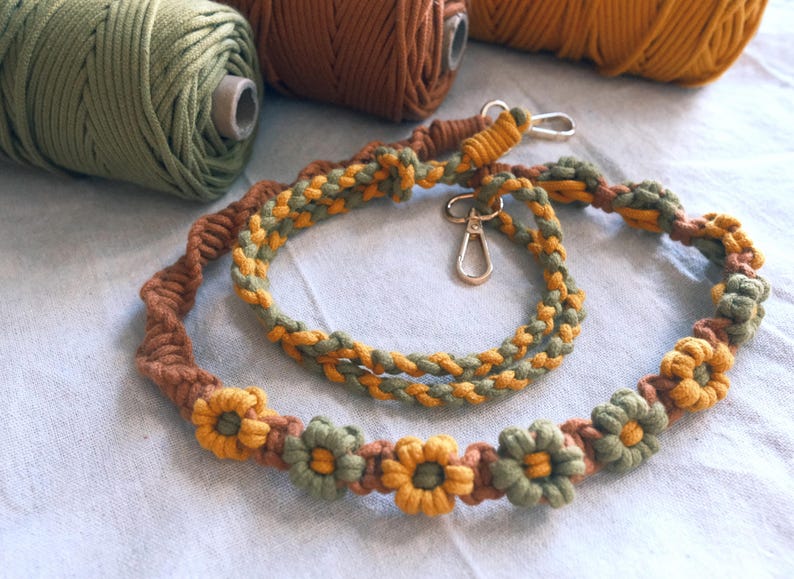 Pu&ograve; includere: Un cordoncino intrecciato verde, marrone e giallo con una chiusura in metallo e dettagli floreali. Il cordoncino &egrave; in cotone e misura circa 76 cm di lunghezza.