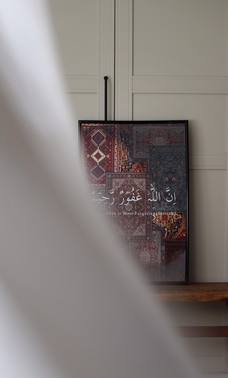 Może przedstawiać: Oprawiona grafika z patchworkowym wzorem wzorzystych dywan&oacute;w w odcieniach czerwieni, błękitu i beżu. Grafika zawiera arabską kaligrafię i angielskie tłumaczenie "Allah is Most Forgiving, Merciful."