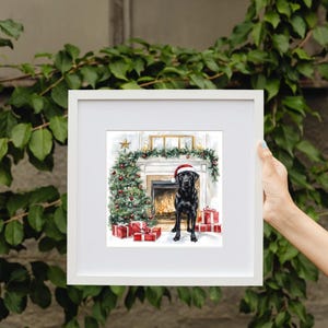 May include: A framed watercolor print featuring a black Labrador wearing a Santa hat, standing in front of a decorated Christmas tree and fireplace. Red wrapped gifts are placed around the dog.