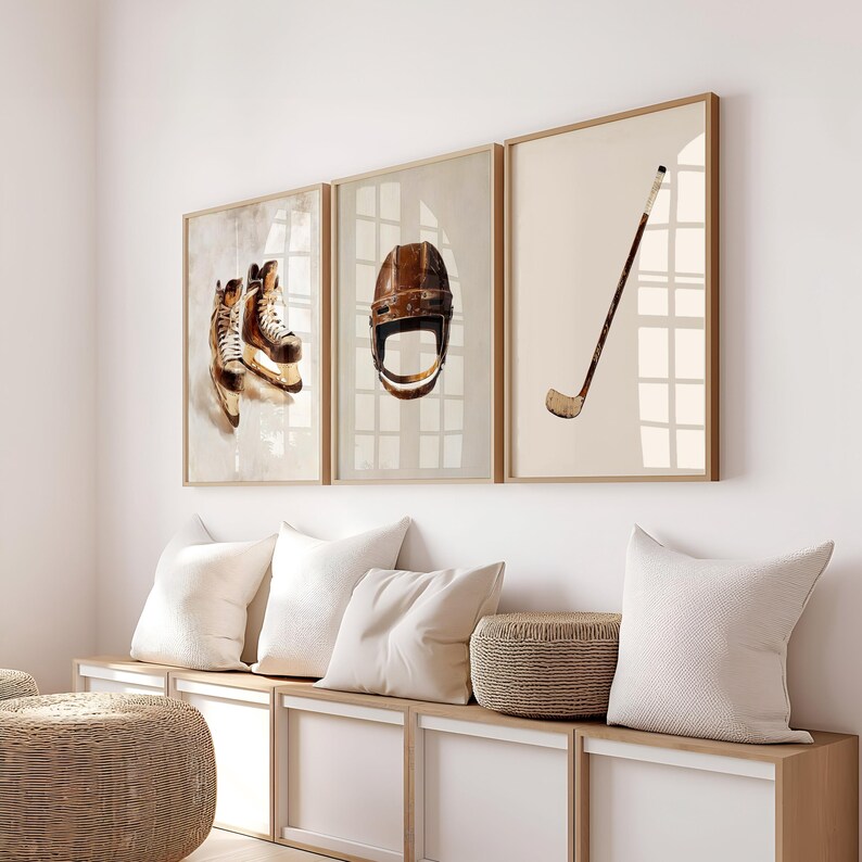 May include: Three framed prints of hockey equipment, including a pair of brown and white ice skates, a brown hockey helmet, and a brown hockey stick. The prints are hanging on a white wall above a white bench with brown cushions and a woven basket.