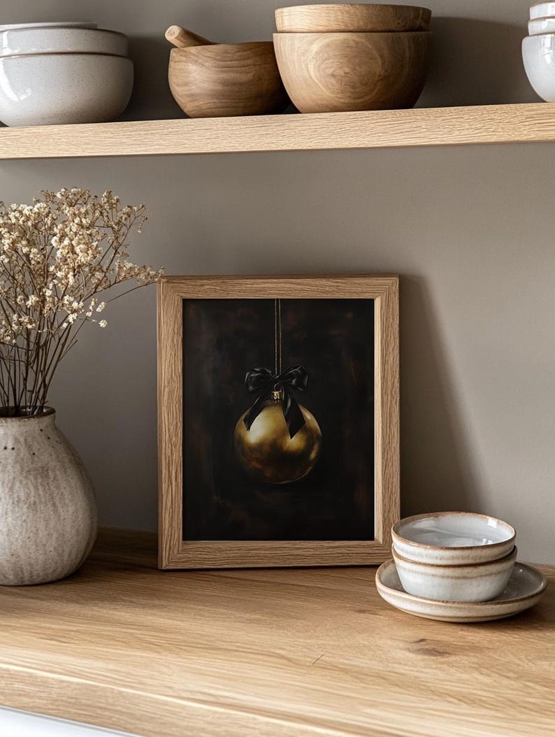 May include: A framed print of a gold Christmas ornament with a black ribbon hanging from a string against a dark background.