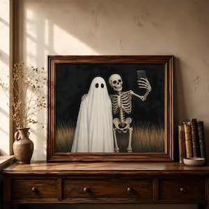 Peut inclure: Une impression d'art encadr&eacute;e repr&eacute;sentant un fant&ocirc;me blanc et un squelette humain c&ocirc;te &agrave; c&ocirc;te sur un fond sombre avec de l'herbe dor&eacute;e. Le squelette tient un smartphone noir pour prendre un selfie avec le fant&ocirc;me, les deux personnages sourient.