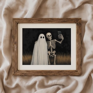 Peut inclure: Une impression d'art encadr&eacute;e repr&eacute;sentant un fant&ocirc;me blanc et un squelette humain c&ocirc;te &agrave; c&ocirc;te dans un champ d'herbes hautes et s&egrave;ches sur fond sombre. Le squelette tient un smartphone noir pour prendre un selfie avec le fant&ocirc;me.