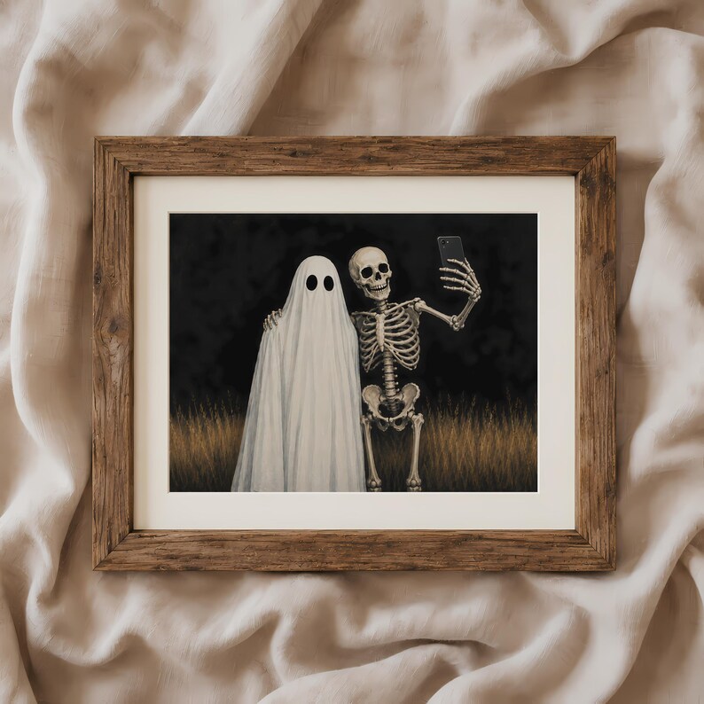 Peut inclure: Une impression d'art encadr&eacute;e repr&eacute;sentant un fant&ocirc;me blanc et un squelette humain c&ocirc;te &agrave; c&ocirc;te dans un champ d'herbes hautes et s&egrave;ches sur fond sombre. Le squelette tient un smartphone noir pour prendre un selfie avec le fant&ocirc;me.
