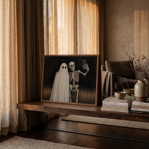 Peut inclure: Une impression d'art encadr&eacute;e rectangulaire repr&eacute;sentant un fant&ocirc;me blanc et un squelette humain c&ocirc;te &agrave; c&ocirc;te dans un champ d'herbes hautes. Le squelette tient un smartphone pour prendre un selfie avec le fant&ocirc;me sur un fond sombre.