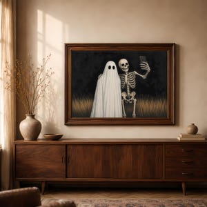 Peut inclure: Une impression d'art mural encadr&eacute;e repr&eacute;sentant un fant&ocirc;me blanc drap&eacute; dans un drap et un squelette humain c&ocirc;te &agrave; c&ocirc;te dans un champ d'herbes hautes la nuit. Le squelette tient un smartphone pour prendre un selfie avec le fant&ocirc;me sur fond sombre.
