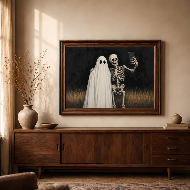 Peut inclure: Une impression d'art mural encadr&eacute;e repr&eacute;sentant un fant&ocirc;me blanc drap&eacute; dans un drap et un squelette humain c&ocirc;te &agrave; c&ocirc;te dans un champ d'herbes hautes la nuit. Le squelette tient un smartphone pour prendre un selfie avec le fant&ocirc;me sur fond sombre.
