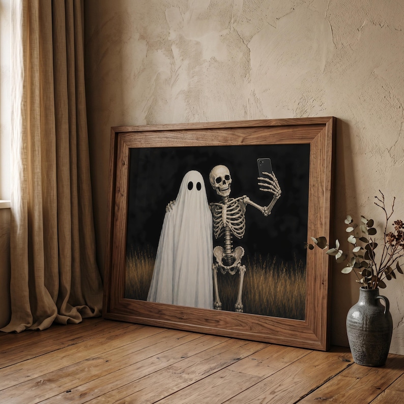 Peut inclure: Une impression d'art murale horizontale encadr&eacute;e repr&eacute;sentant un fant&ocirc;me blanc drap&eacute; dans un drap debout &agrave; c&ocirc;t&eacute; d'un squelette humain. Le squelette tient un smartphone noir pour prendre un selfie. Le fond montre un feuillage sombre et de l'herbe dor&eacute;e.