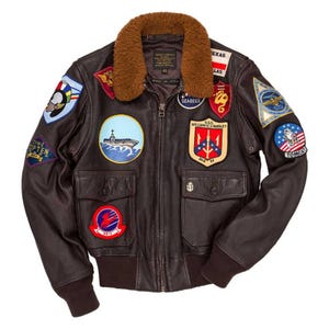 Può includere: Giacca bomber in pelle marrone con colletto in finta pelliccia marrone. La giacca presenta diverse toppe ricamate, tra cui disegni militari e a tema aeronautico. Ha due tasche frontali e una chiusura con cerniera. Taglia giacca: 40.